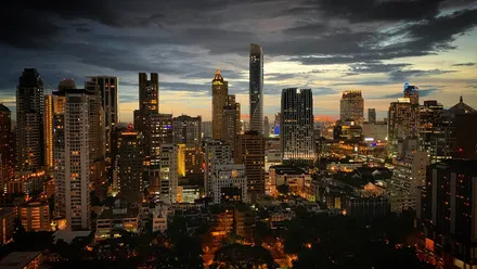 The rooftop at dusk, Bangkok skyline behind, a few people sitting on cushions with their backs to the camera.